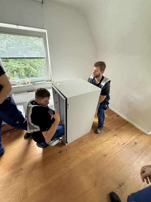 Zwei Kollegen bringen ein weißes Einbaugerät durch ein leeres Zimmer