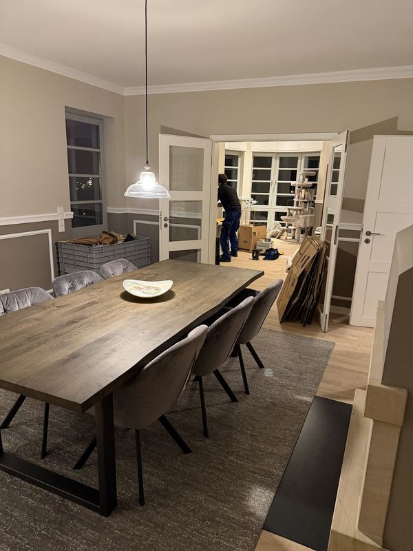 Ein fertig eingerichtetes Esszimmer, der Tisch ist gedeckt, nebenan werden leere Kartons zusammengefaltet