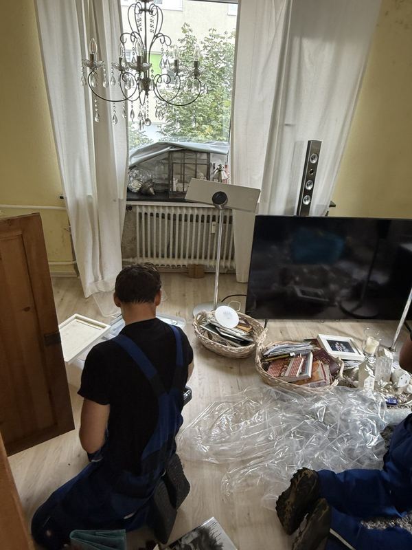 Auf dem Boden kniend sortiert ein Kollege Hausrat aus Kisten und Körben