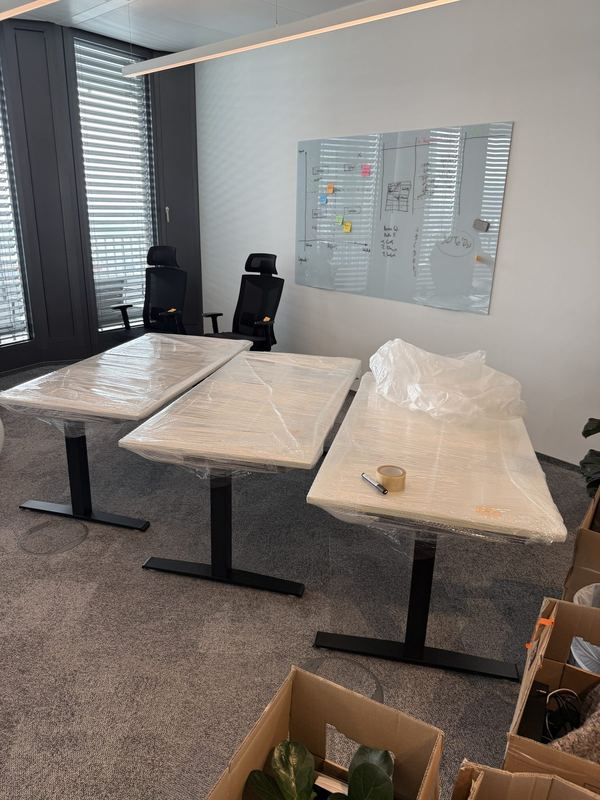Nebeneinander stehen drei höhenverstellbare Schreibtische im Büro, ihre Platten sind foliert