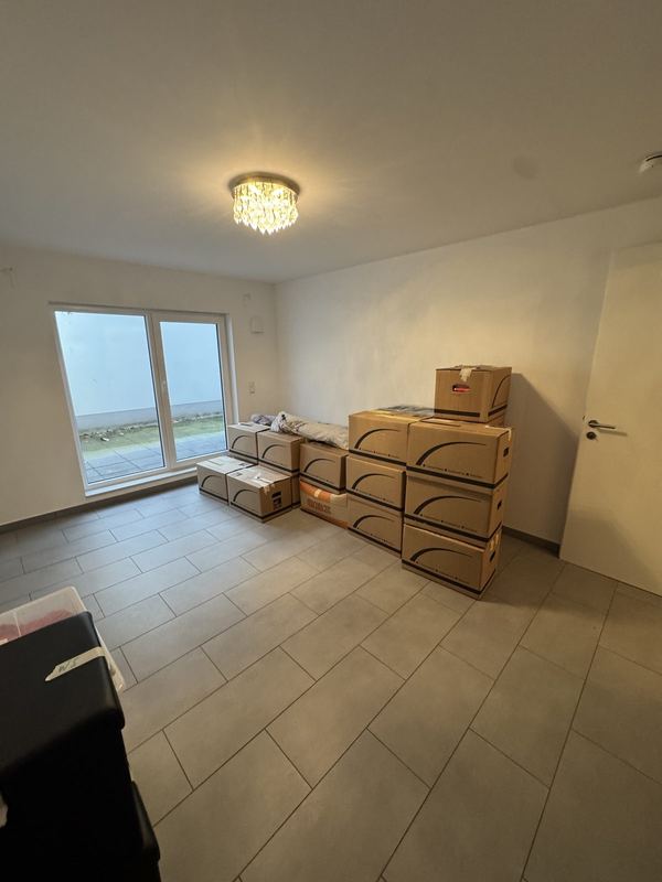 Umzugskartons stehen gestapelt in einem leeren Zimmer eines Neubaus mit bodentiefem Fenster