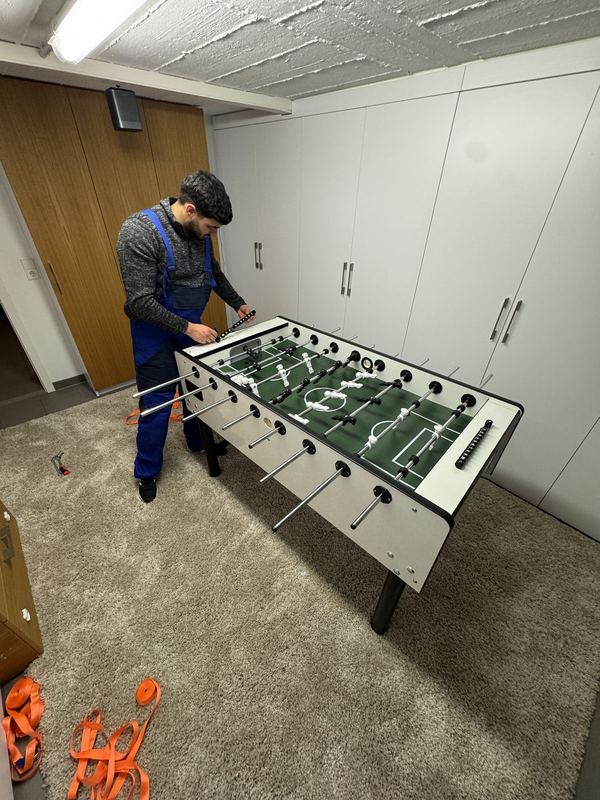 In einem Kellerraum montiert ein Kollege die Spielstangen eines Tischkickers