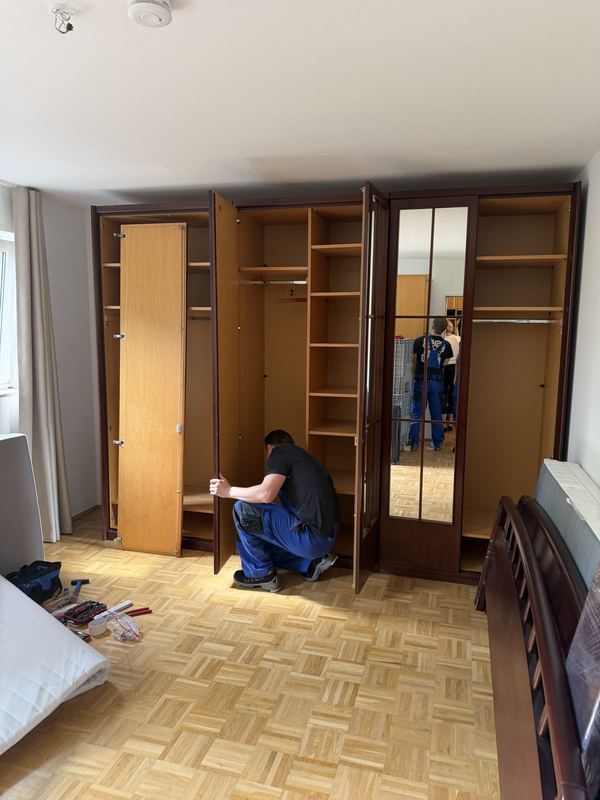 In einem Schlafzimmer justiert ein Kollege die Türen eines Kleiderschranks mit mehreren Türen