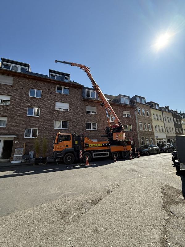 Ein orangefarbener Kranwagen mit ausgefahrenem Ausleger steht in einer Wohnstraße, abgesichert mit Warnkegeln