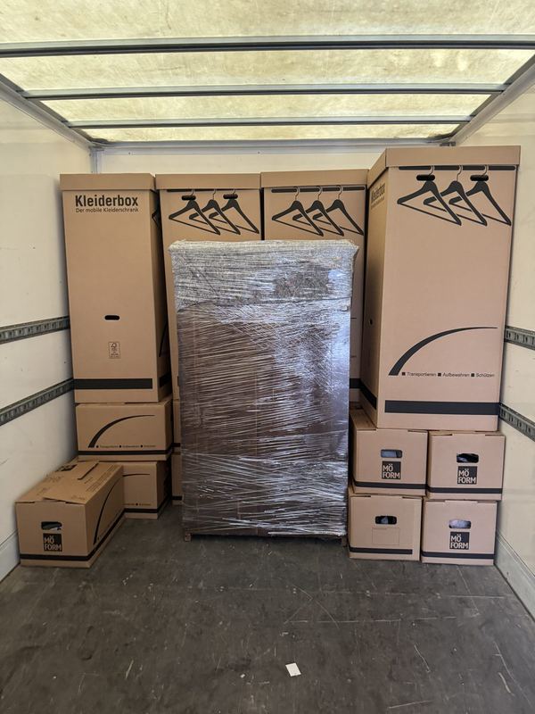 Im Laderaum stehen Kleiderboxen in einer Reihe, mittig ein in Folie verpackter Schrank