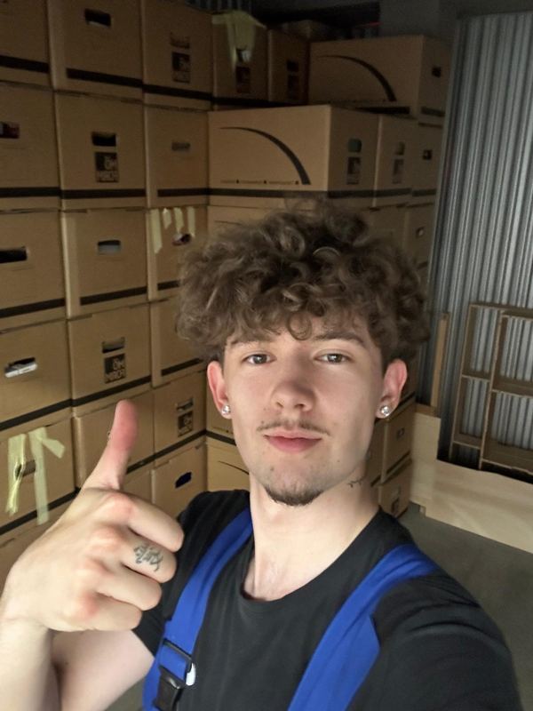 Vor einem Stapel fertig gepackter und beschrifteter Umzugskartons steht ein Kollege