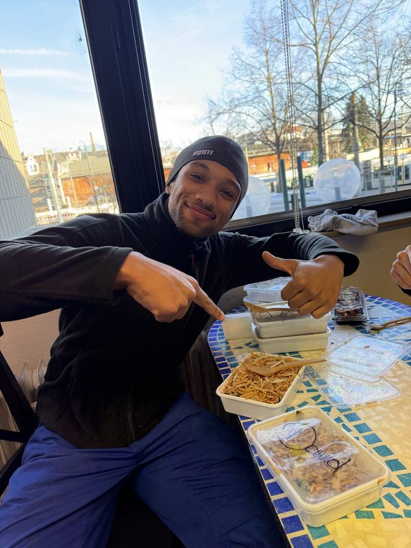In der Mittagspause sitzt ein Kollege am Tisch und deutet auf sein Essen