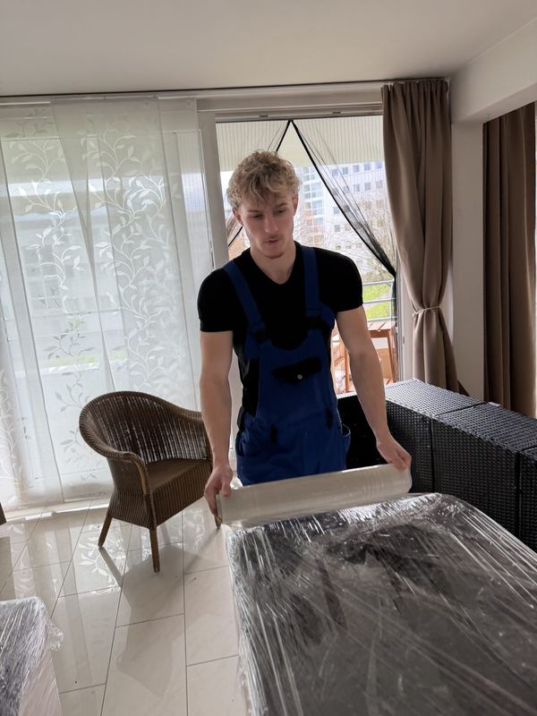 In einer Wohnung wickelt ein Kollege Stretchfolie um ein Möbelstück