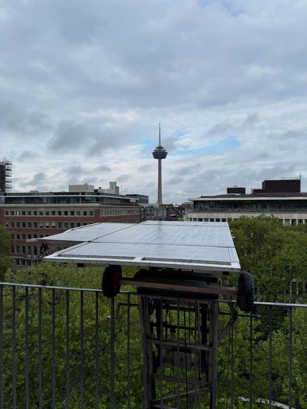 Auf Höhe eines oberen Stockwerks schwebt die Plattform eines Möbellifts, hinten ein Fernsehturm