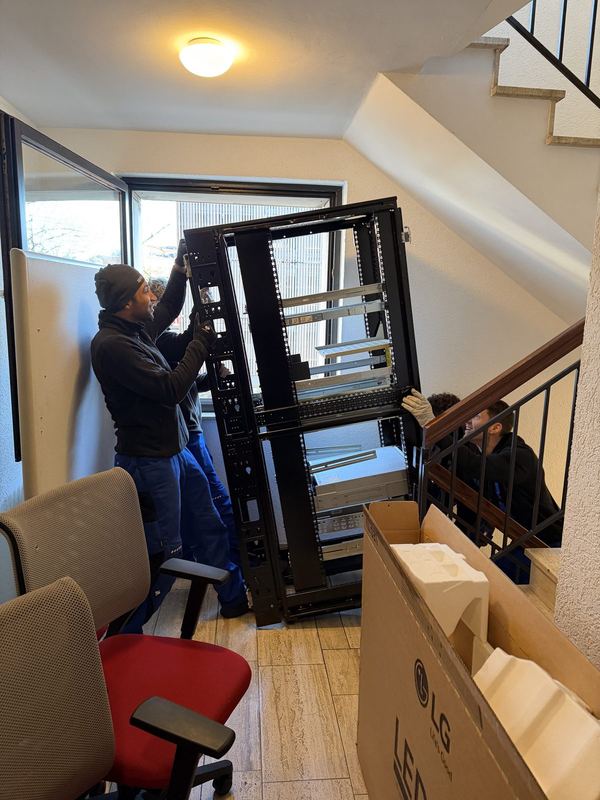 Drei Kollegen bringen einen offenen Serverschrank durch ein Treppenhaus nach unten