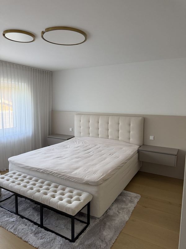 Fertig eingerichtetes Schlafzimmer am Zielort In einem hellen Schlafzimmer steht ein fertig montiertes Bett mit hellem gepolstertem Kopfteil, hängenden Nachtkonsolen und einer Sitzbank