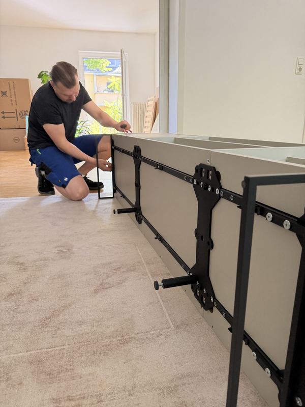 Vor einem liegenden Sideboard kniet ein Kollege und bringt die Beschläge an