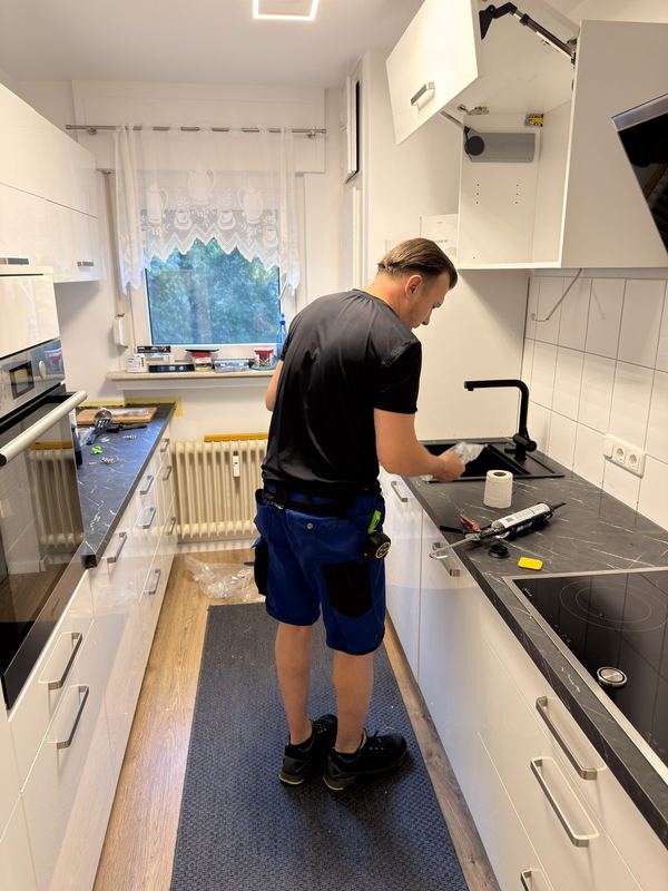 Eine schwarze Spüle wird von einem Monteur in den vorbereiteten Ausschnitt der Arbeitsplatte eingesetzt