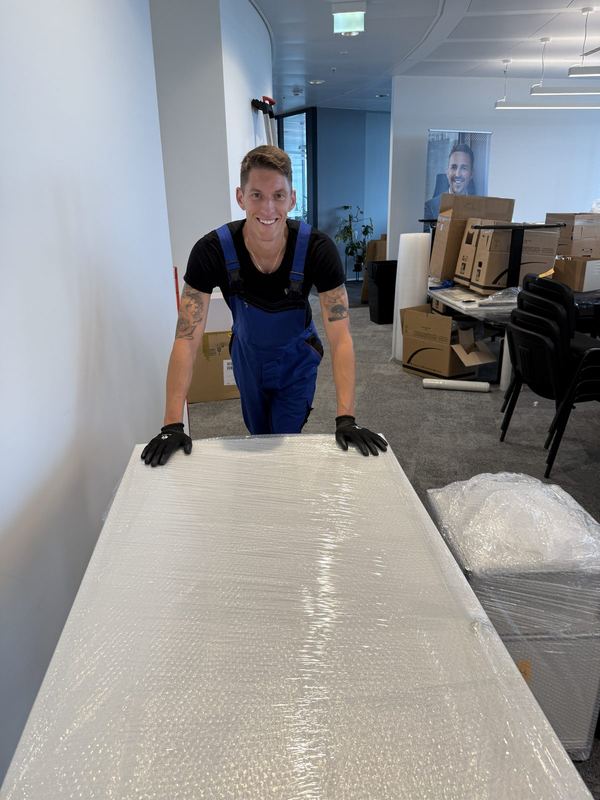 Hinter einer vollflächig mit Luftpolsterfolie eingepackten Tischplatte steht ein Kollege