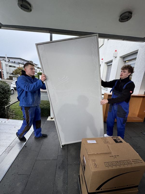 Zwei Kollegen bringen eine große weiße Platte hochkant zum Fahrzeug