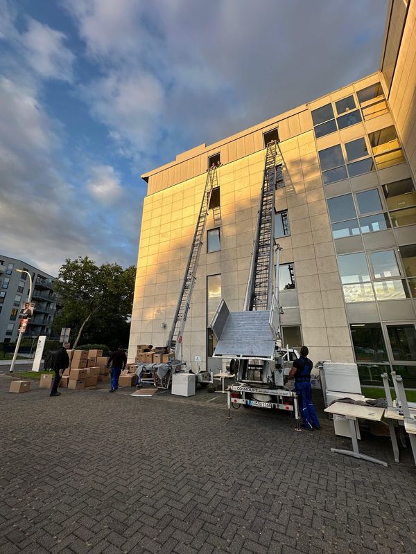 Vor der Fassade eines Bürogebäudes stehen zwei ausgefahrene Möbellifte nebeneinander