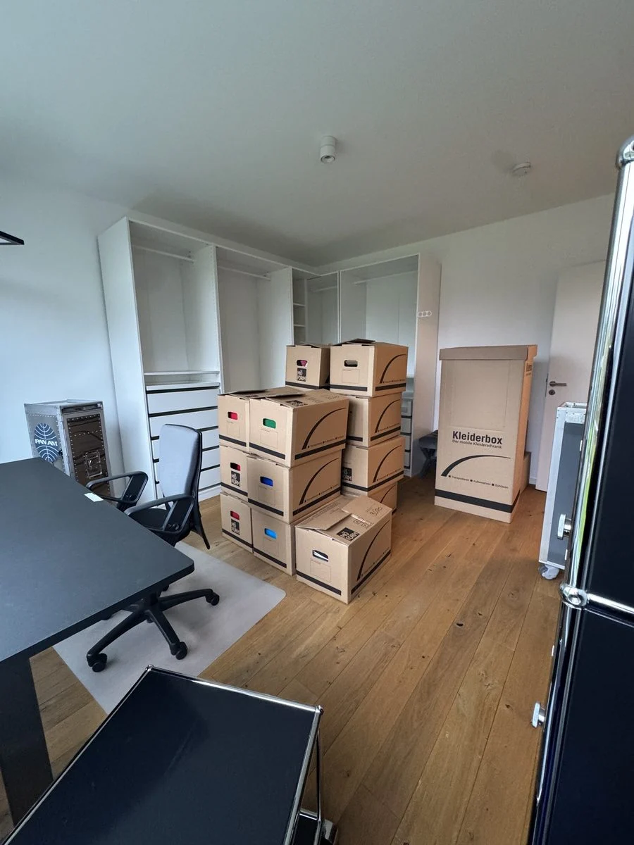 Büro mit gestapelten Umzugskartons und einem Rollcontainer am Fenster