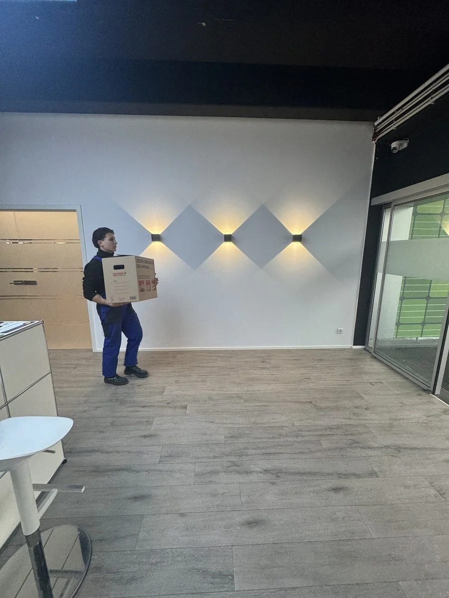 Ein Kollege trägt einen Karton durch einen leeren, offenen Loft-Raum