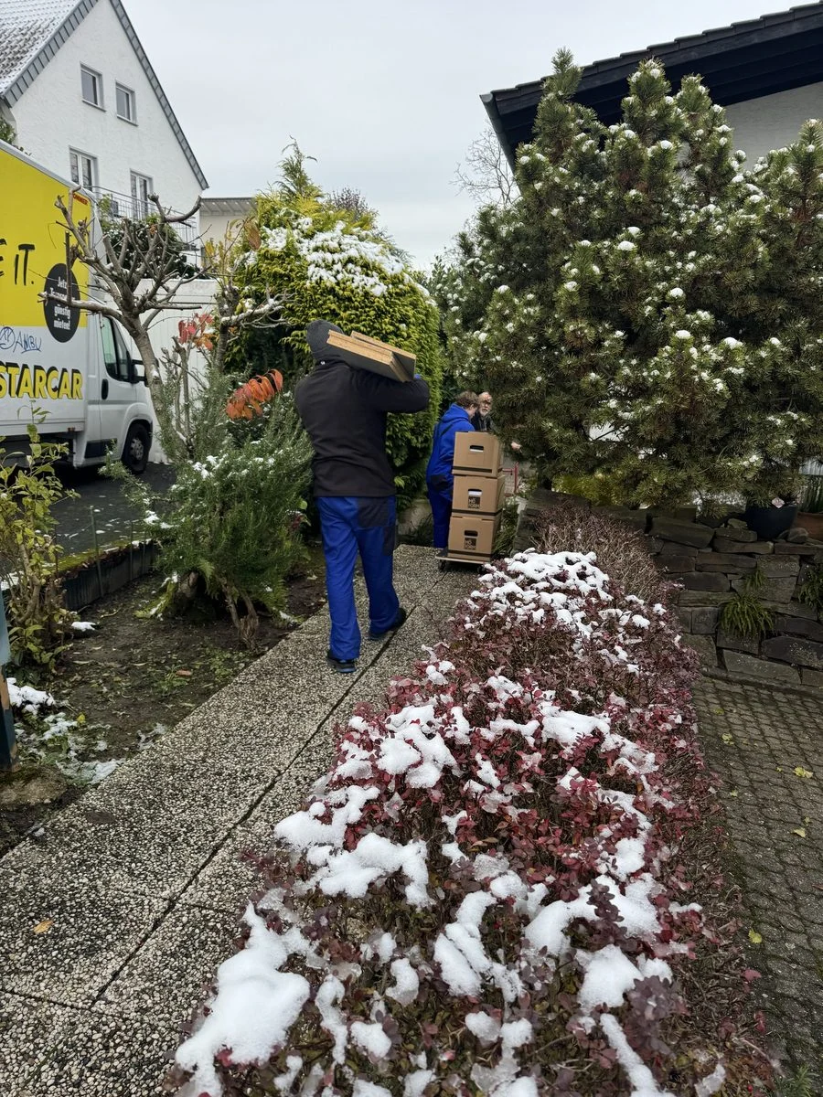 Ein Umzugshelfer trägt einen Karton durch einen verschneiten Garten zum Haus