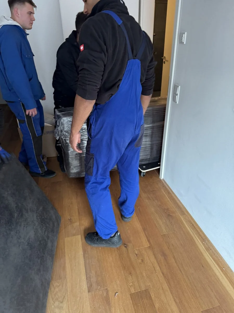 Zwei Umzugshelfer in Arbeitskleidung tragen Kisten durch einen Flur