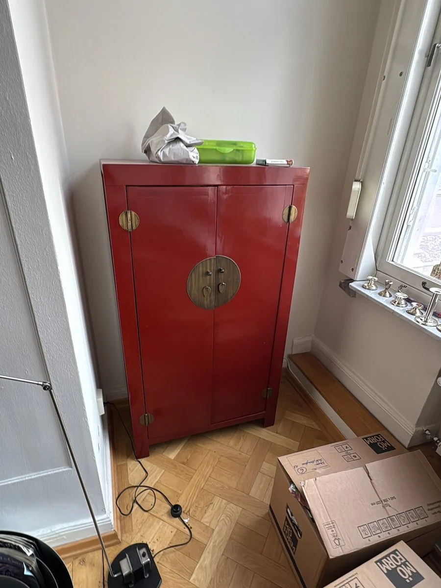 Roter antiker Lackschrank steht in einem Altbauzimmer, davor gepackte Kartons
