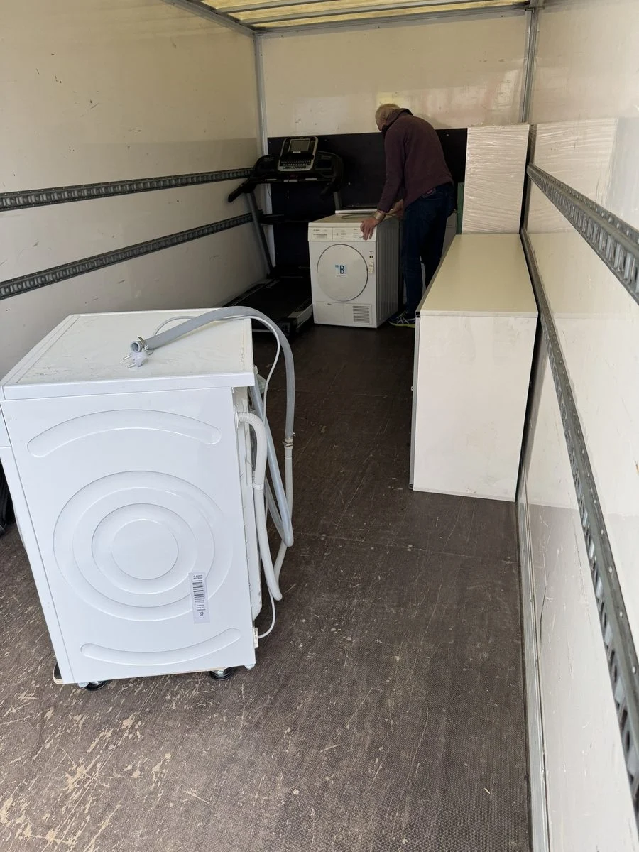 LKW-Laderaum mit Waschmaschine und Kisten, im Hintergrund steht ein Kollege