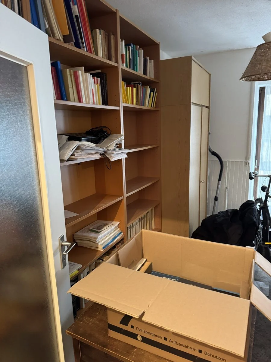 Regalwand mit einem geöffneten, leicht unaufgeräumten Umzugskarton davor