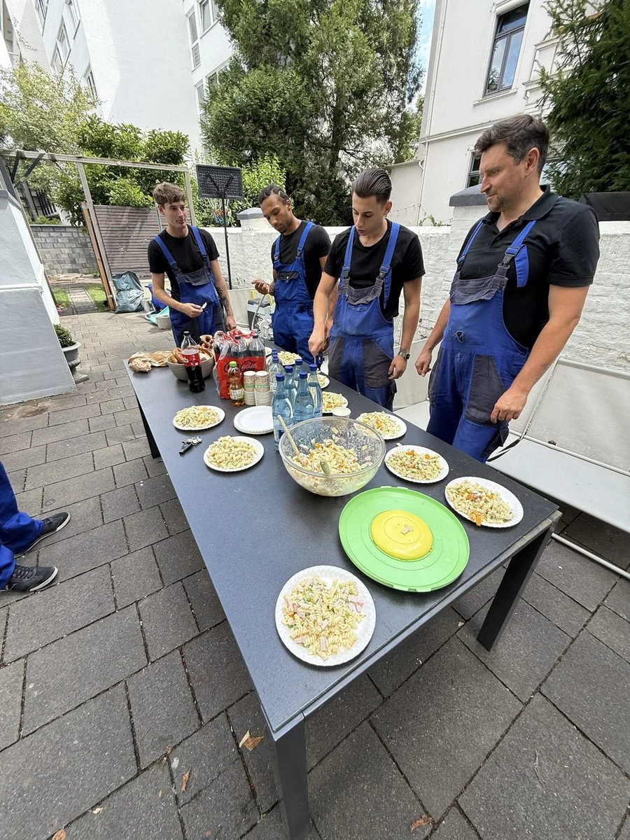Das Team in Arbeitskleidung beim gemeinsamen Essen an einem Tisch im Freien