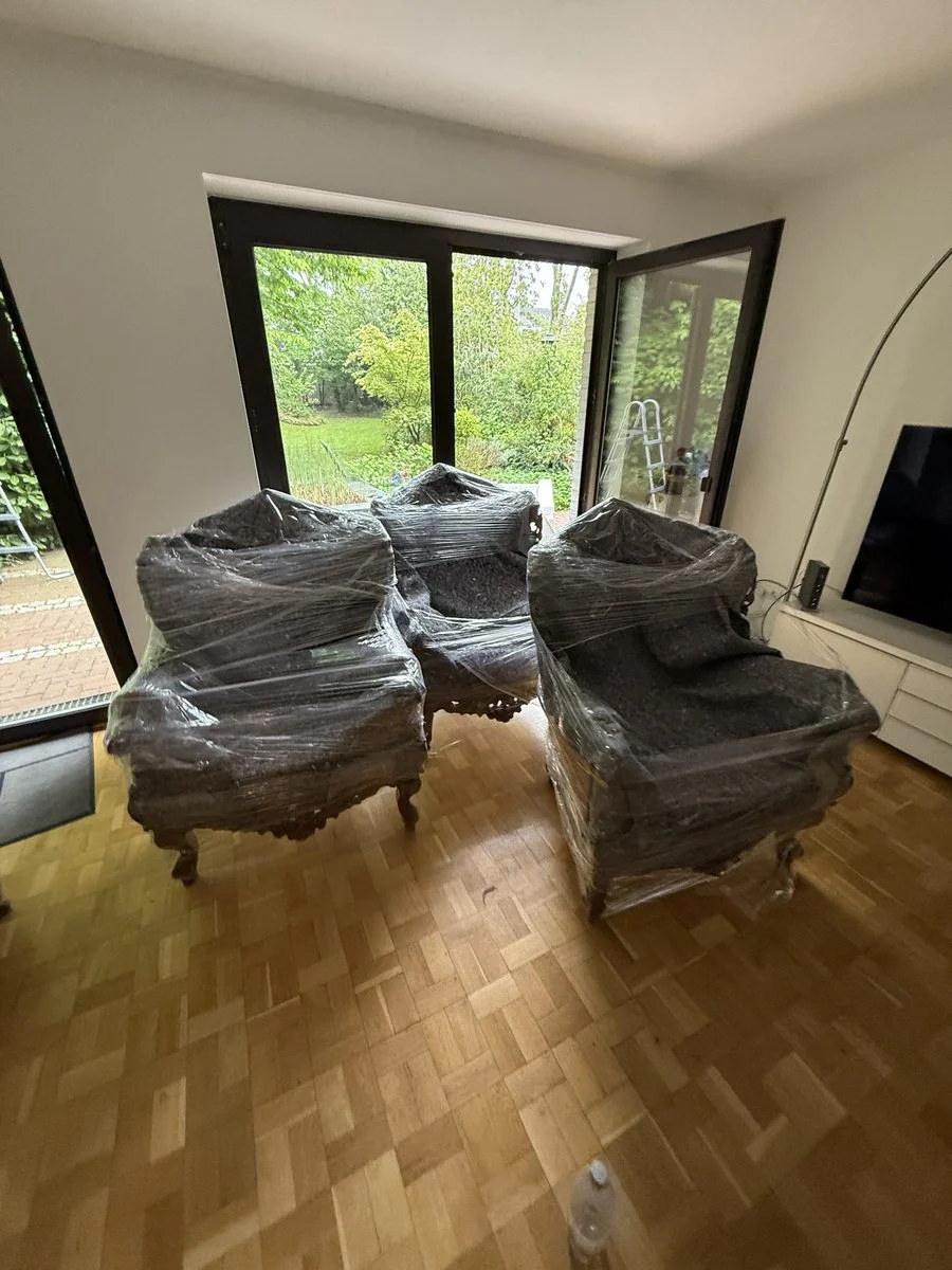 Wohnzimmer mit vier verpackten Sesseln im Kreis vor großen Fenstern