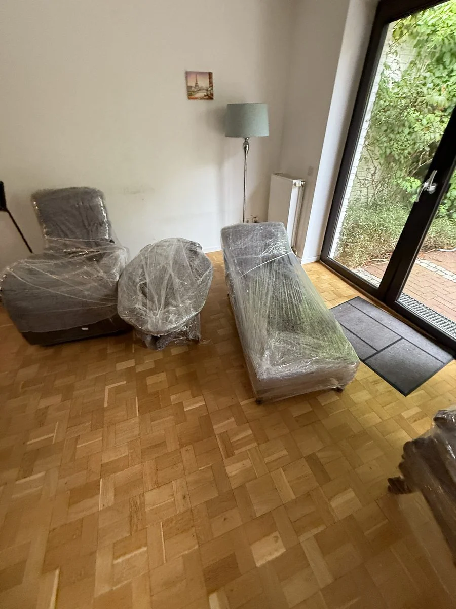 Wohnzimmer mit zwei verpackten Möbelstücken und einer Stehlampe