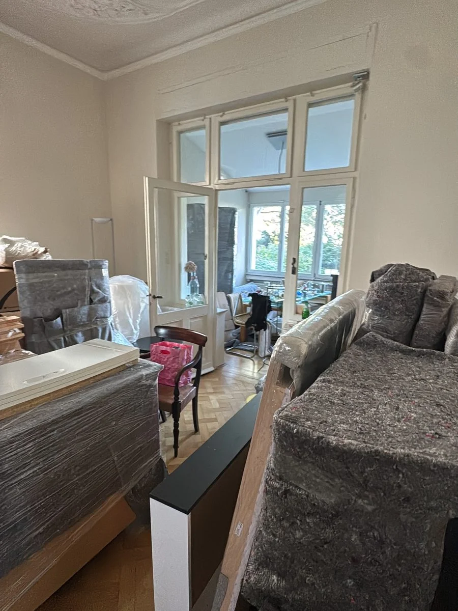 Wohnzimmer einer Altbauwohnung, die Möbel sind vor dem Transport in Schutzfolie eingepackt